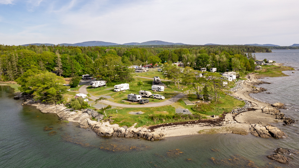 An arial shot of a KOA campground on the coast of the water with tons of trees surrounding it 