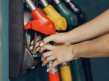 Hands reach and grab one of four fuel pumps at a gas station