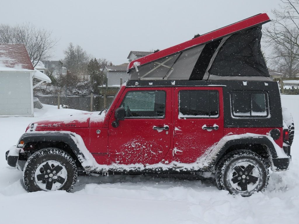A jeep camper popped up on a red Jeep in the snow 