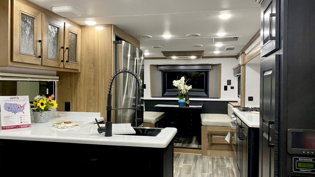 Interior shot of a fifth wheel kitchen with a dinette booth, fridge, and sink 