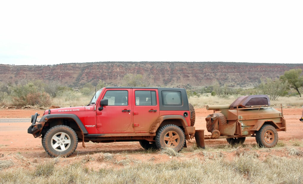 A red Jeep towing a small trailer to go camping with 