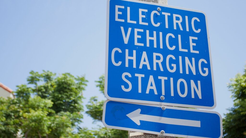 A blue sign with white lettering that says "electric vehicle charging station" and an arrow pointing to the left