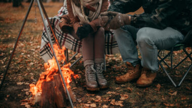A couple sitting together by the fire in their oversized camping chairs.