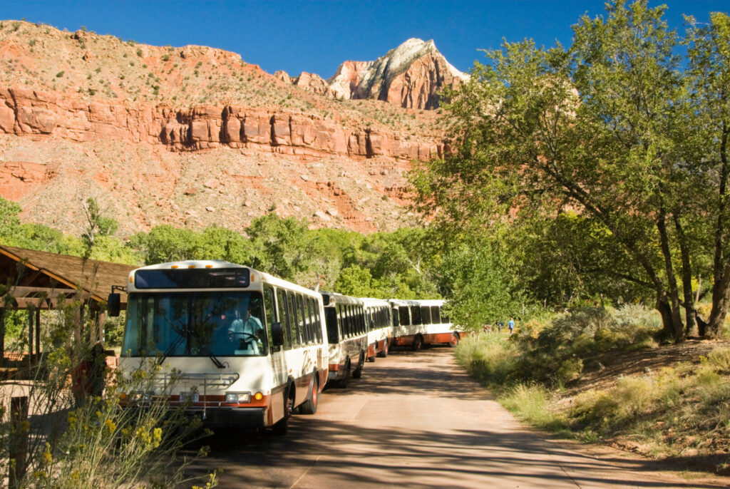 A propane fueled shuttle bus stops at the Visitor's Center in Zion National Park in southwest Utah. Sandstone formations in the background. 