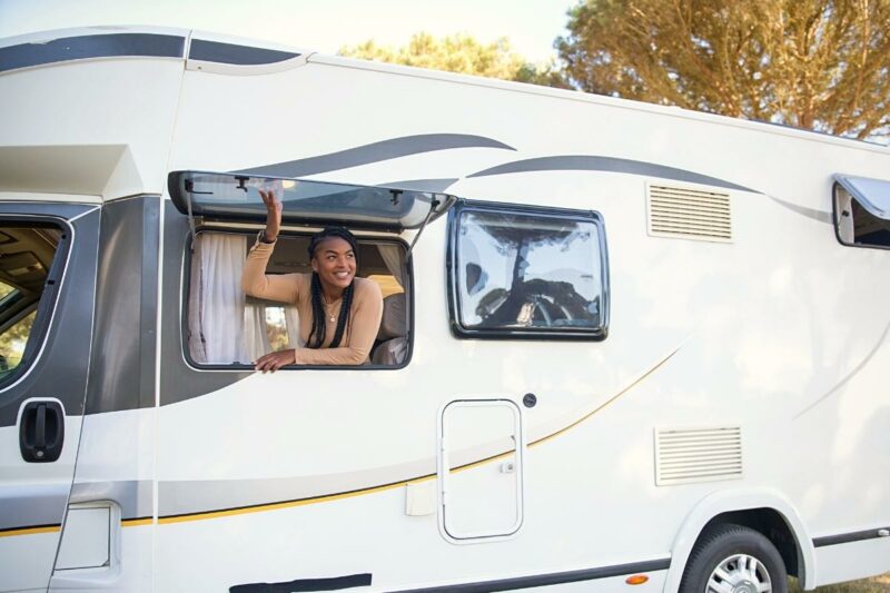 A woman smiles as she joyfully looks out of her RV window at her campground.