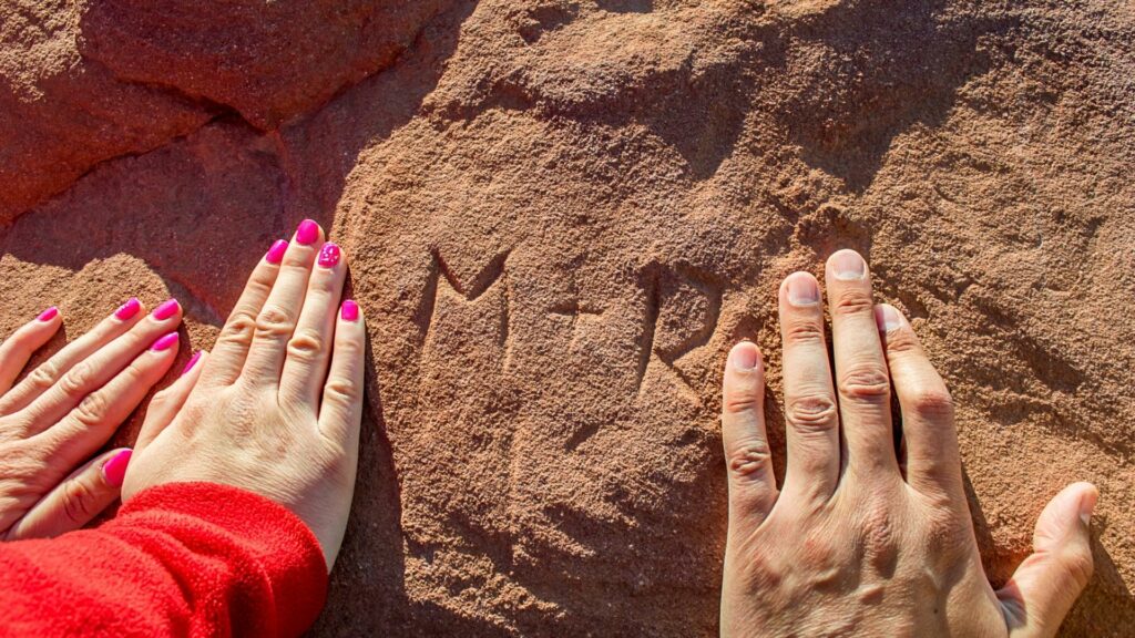 A couple pushing their hands against a rock that they carves their initials into. This is breaking national park rules and can even be fined for.