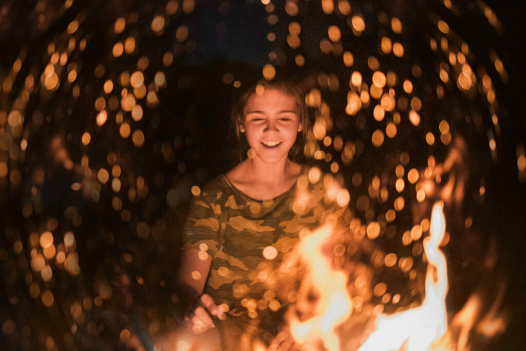 A girl looking into a fire while camping after using fire color changer.