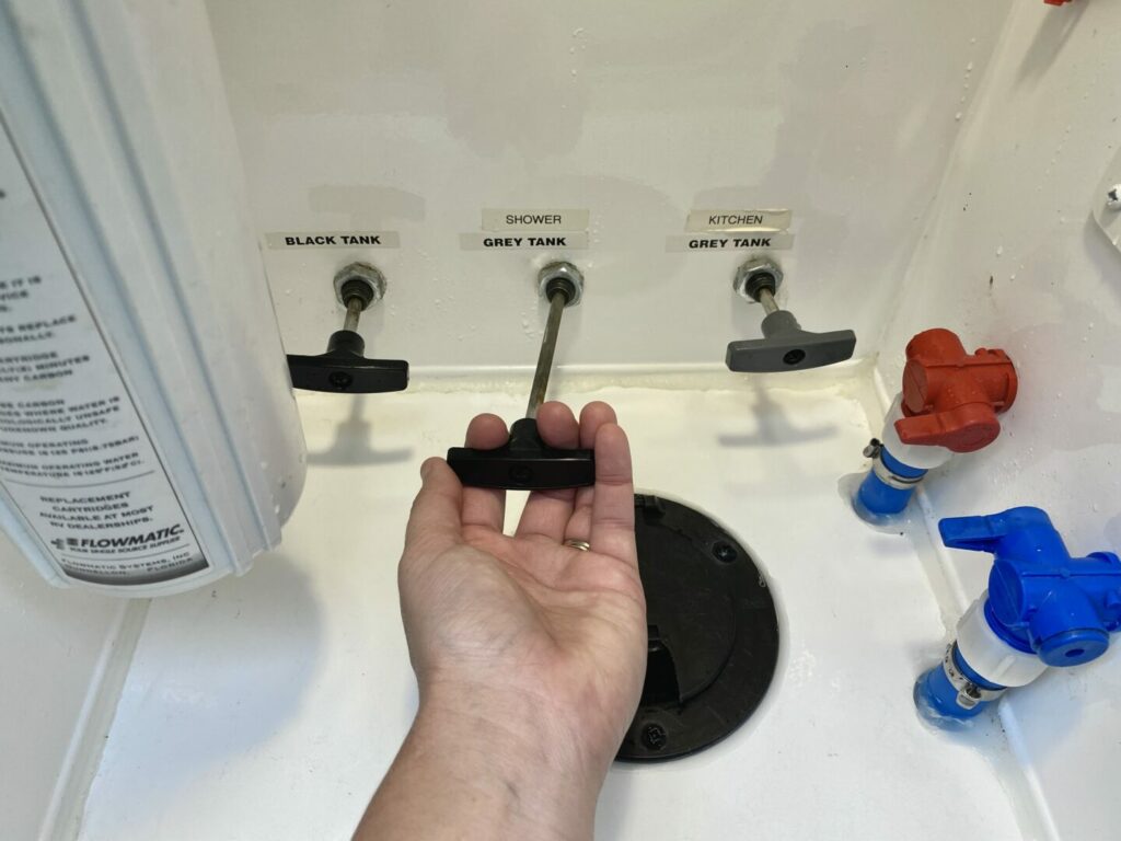 The black and grey tank valves of an RV with a hand pulling one open