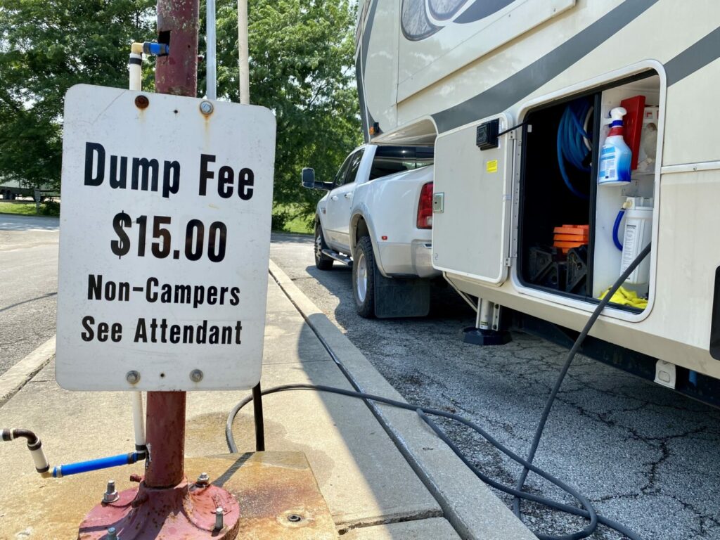 An RV at a dump station hooked up to the water and a sign saying that there is a $15 dump fee