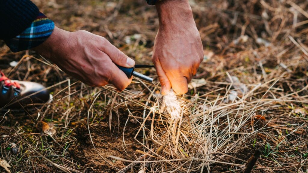 A man using a fire starters for camping that sparking over a pile of dead grass
