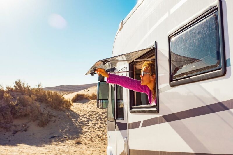A woman opens the window on her RV on a hot sunny day in the desert