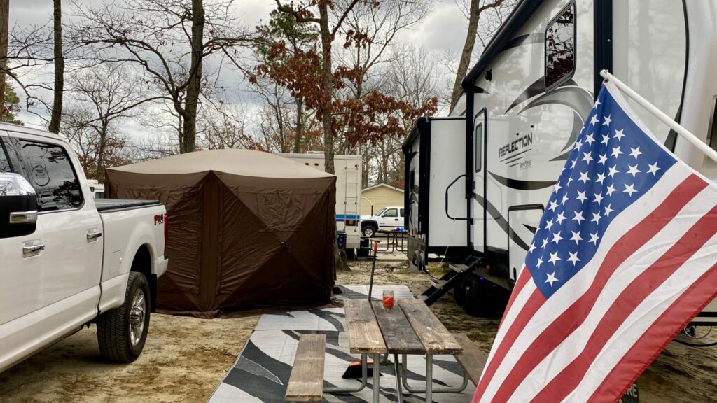 A screen tent setup in a campsite with an RV, truck, and USA flag flying next to it