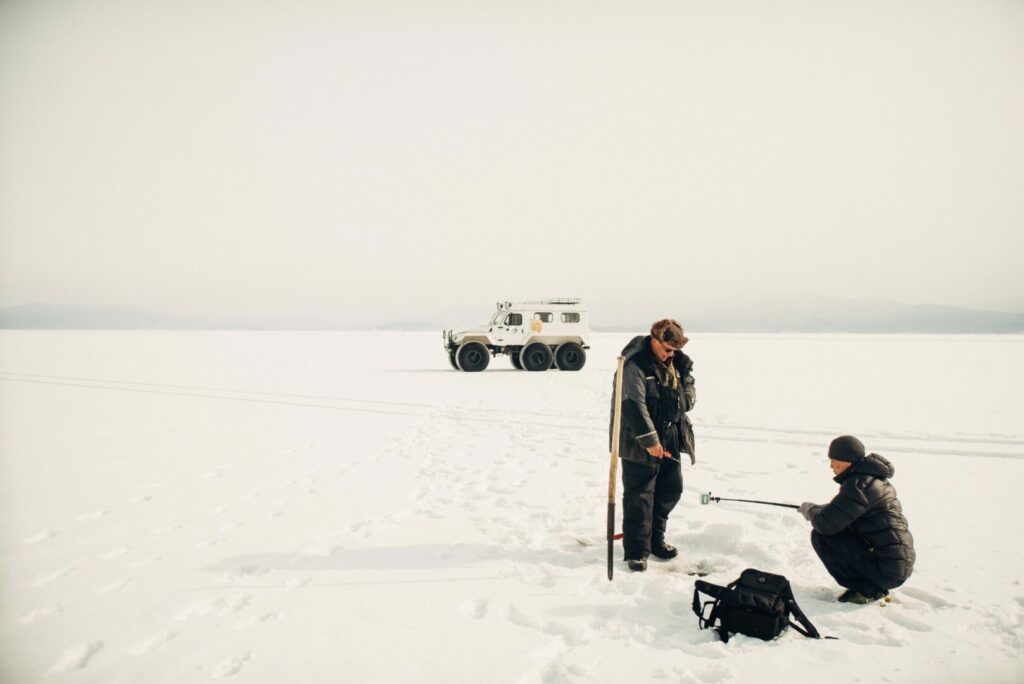 Two fishermen ice fishing with their trailer.