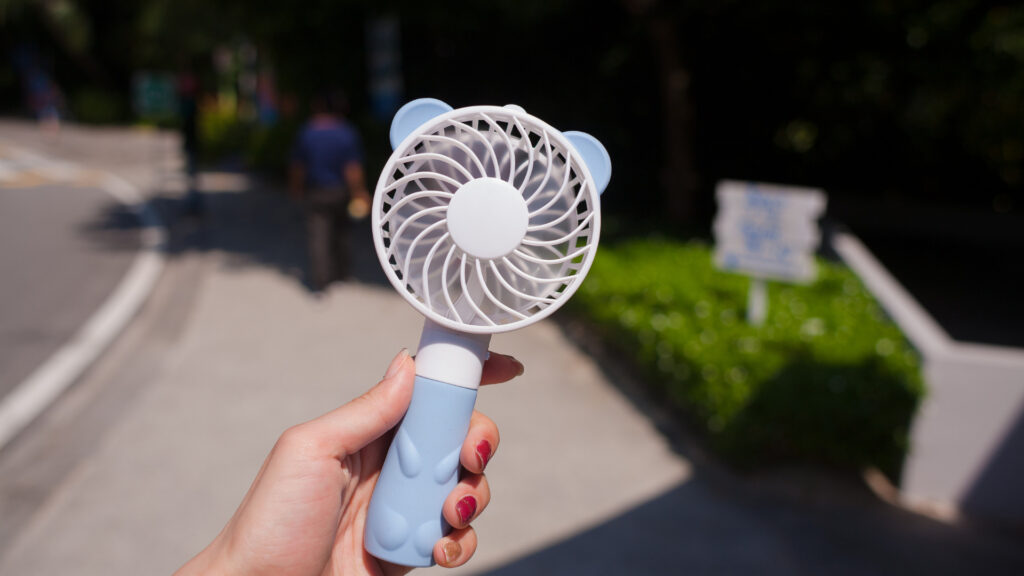 A person holding a battery powered fan.