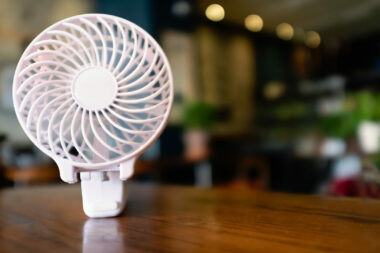 Close up of a portable battery operated fan, folded on a wooden table.