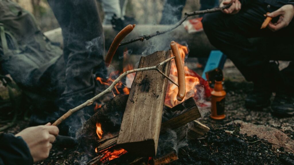 People roasting hot dogs on sticks over a campfire 