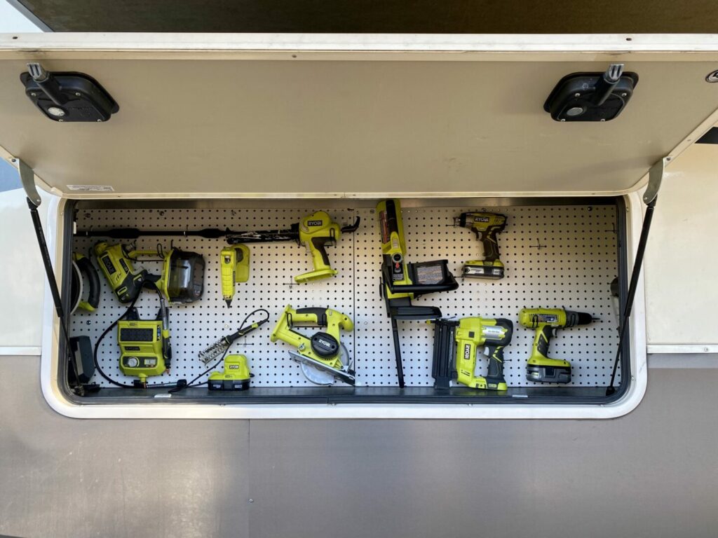 An RV storage door open to show a peg board with loads of bright green tools organized in there 