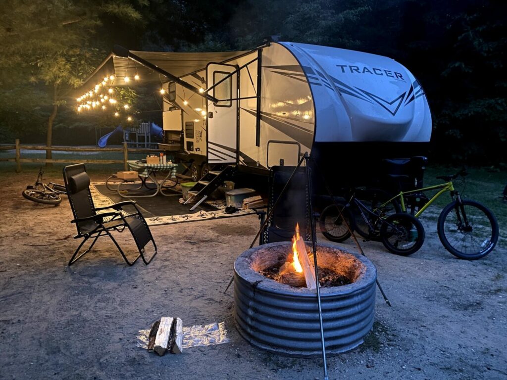 A travel trailer site with a campfire, chairs, and string lights setup at Warren Dunes State Park.
