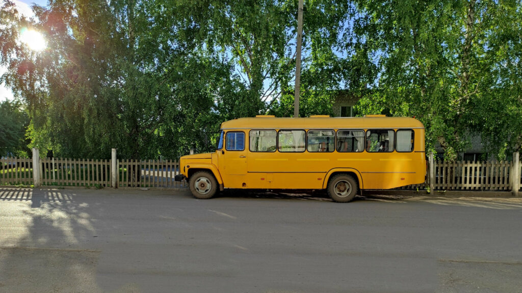 A yellow skoolie bus in front of a house on a tree lined street.