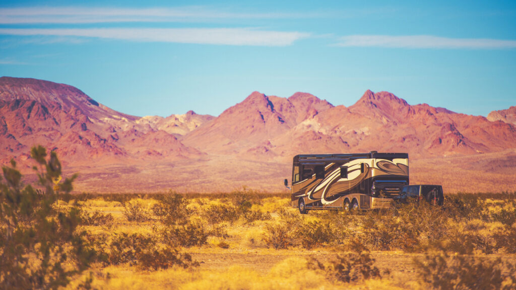 A diesel pusher motorhome boondocking out in the desert with a view of barren mountains.