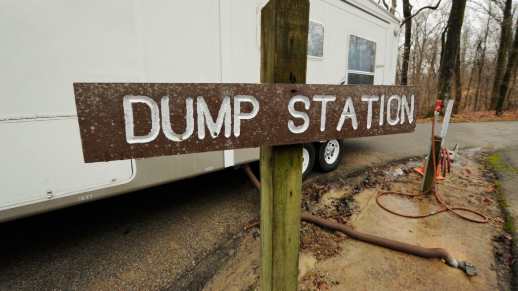 A wooden sign that says "dump station" with an RV connected to it in the background
