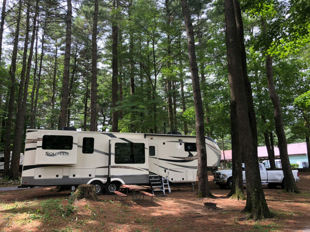 A fifth wheel parked in a first come first serve camping spot in upstate New York with lots of trees