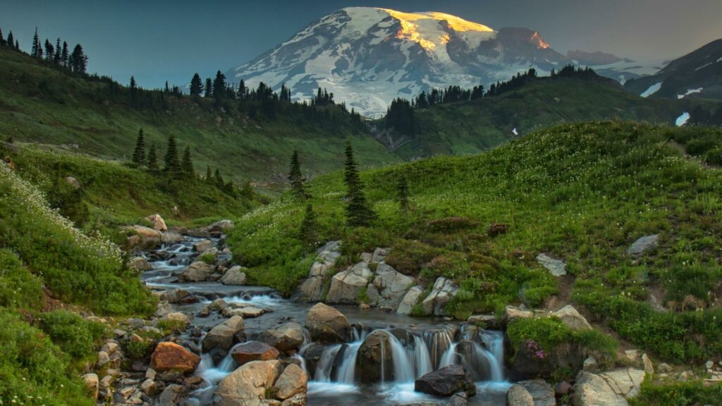 A river running through lush green hills with the towing Mount Rainier covered in the snow in the background. 