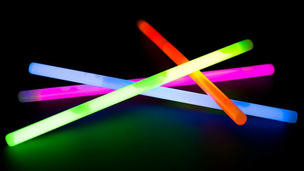 Four glow sticks stacked on top of each other on a black background. Glow sticks on your tent is one of the many camping hacks you should try.
