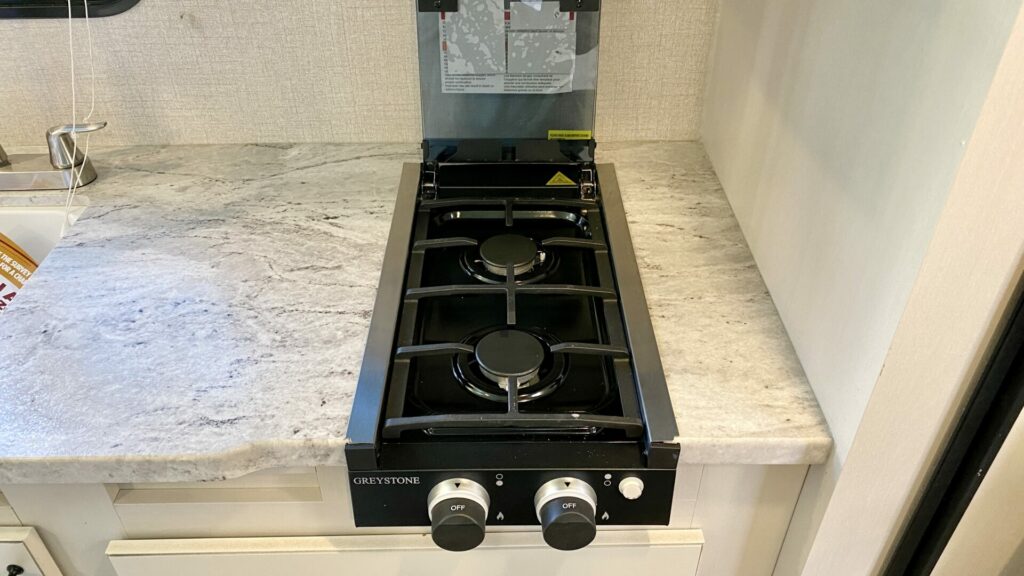 A two burner Greystone brand RV stove top installed in a small RV with fake granite countertop 