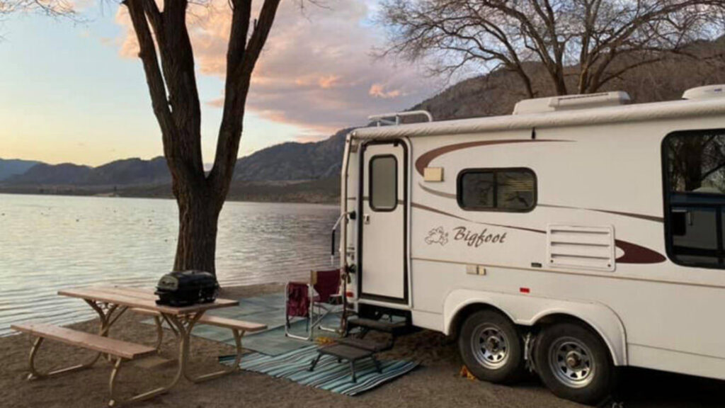 A bigfoot RV camper parked by the water at a campsite.