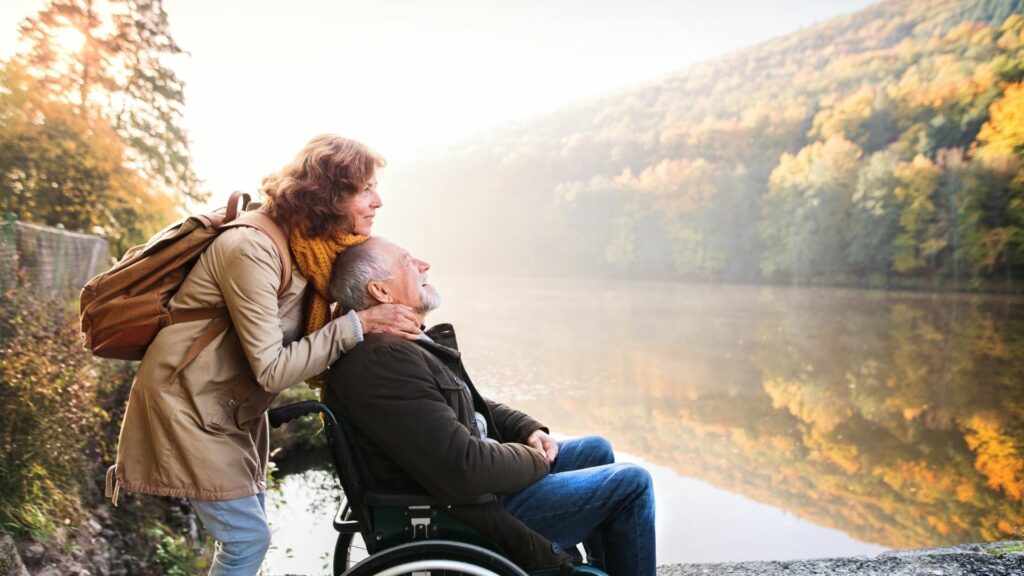 A man in a wheelchair enjoying a walk through a national park overlooking a river with his wife.