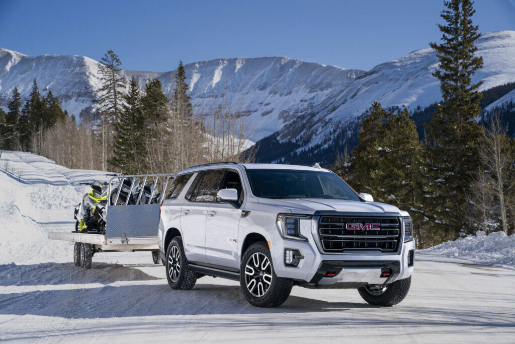 A GMC Yukon towing snowmobiles on a trailer in the snowy mountains 