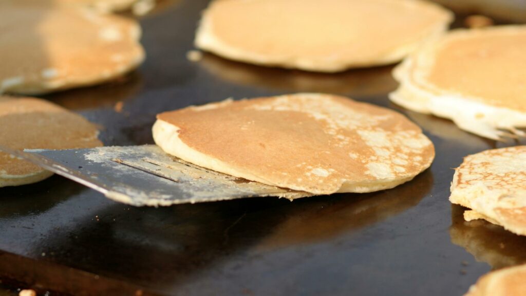 Pancakes cooking on a Blackstone Griddle with one getting flipped by a spatula 