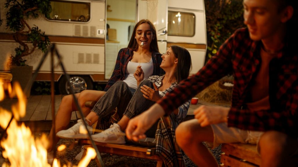 Girls eating marshmallows around a campfire with an RV in the background