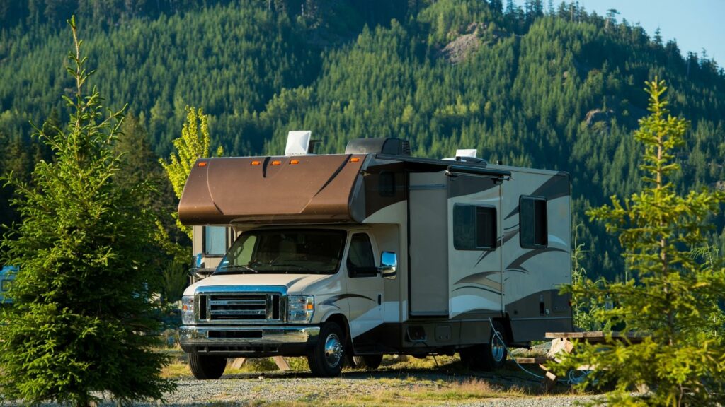 A brown Class C RV parked in a campsite with trees and mountains in the background 