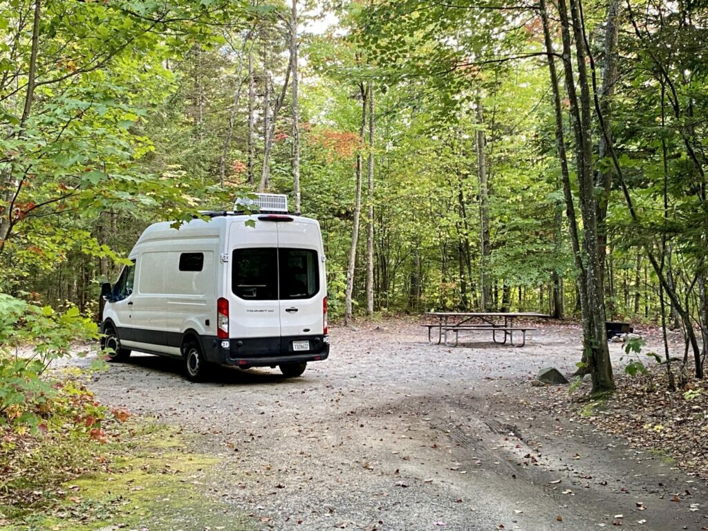 A van parked in a campsite with nothing setup outside and no one around 