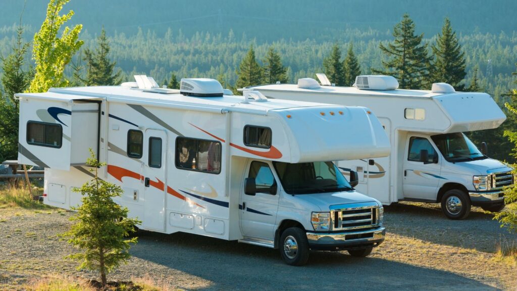 Two class C motorhomes parked in a campground in the mountains with tons of trees