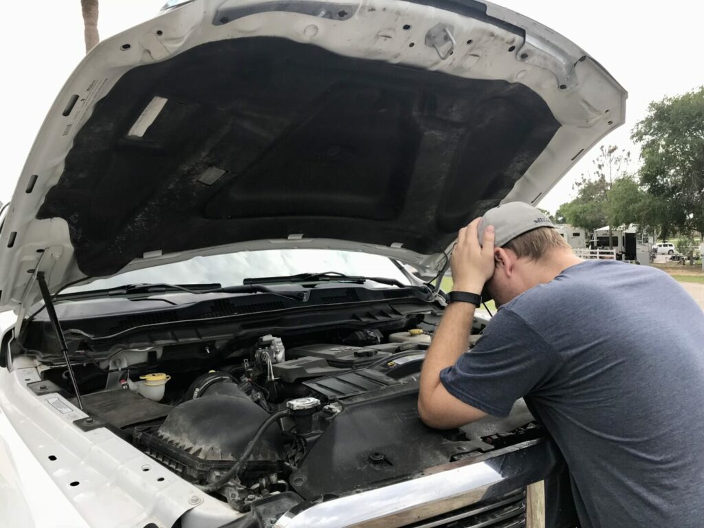 A man leaning over his engine with his hands on his head 