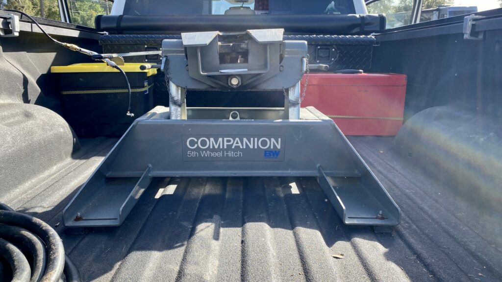 A 5th wheel hitch installed in the back of a white RAM truck with camping accessories in the bed of the truck