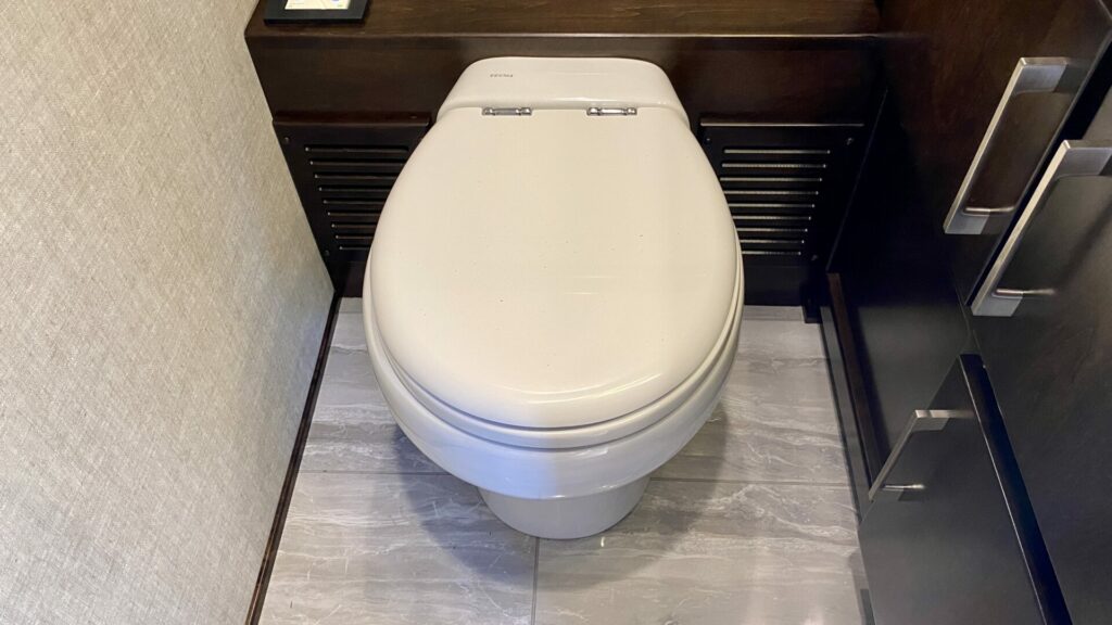 A fancy RV toilet with an RV bidet that is the whole seat cover in a dark brown bathroom