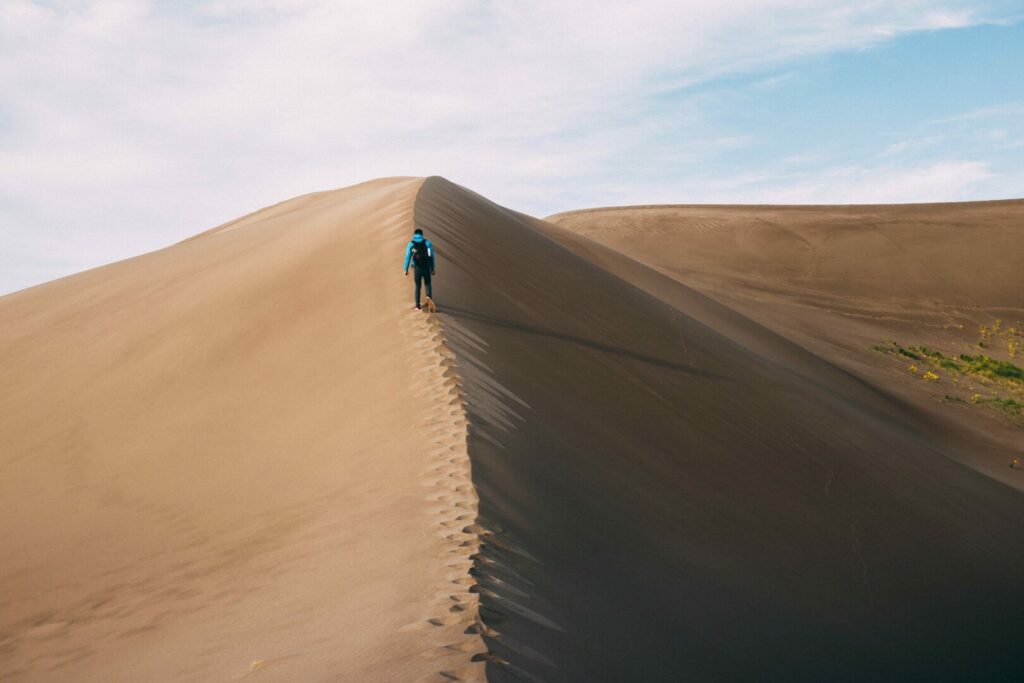 A man traveling in the Sand Dunes in Colorado. Colorado is well known for their national parks and is not a state with no national parks.