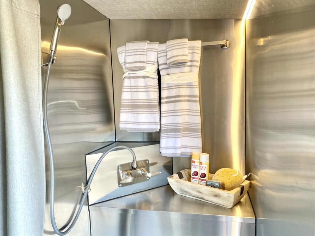 An RV wet bath with stainless steel walls and two towels hanging up by the shower head 