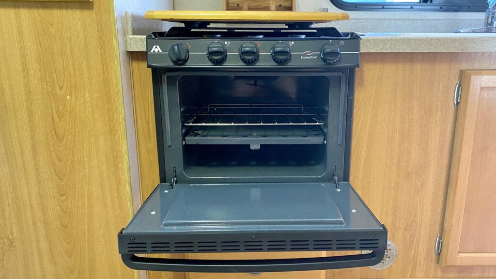 A propane RV stove with the oven door open showing the rack at the bottom level 