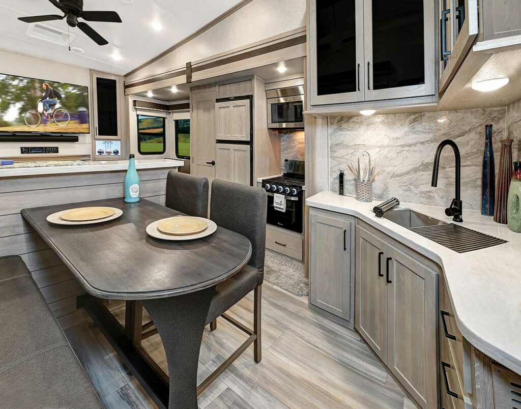 Interior shot of a fifth wheel by Rockwood Campers showing the kitchen, dinette, and TV in the background 