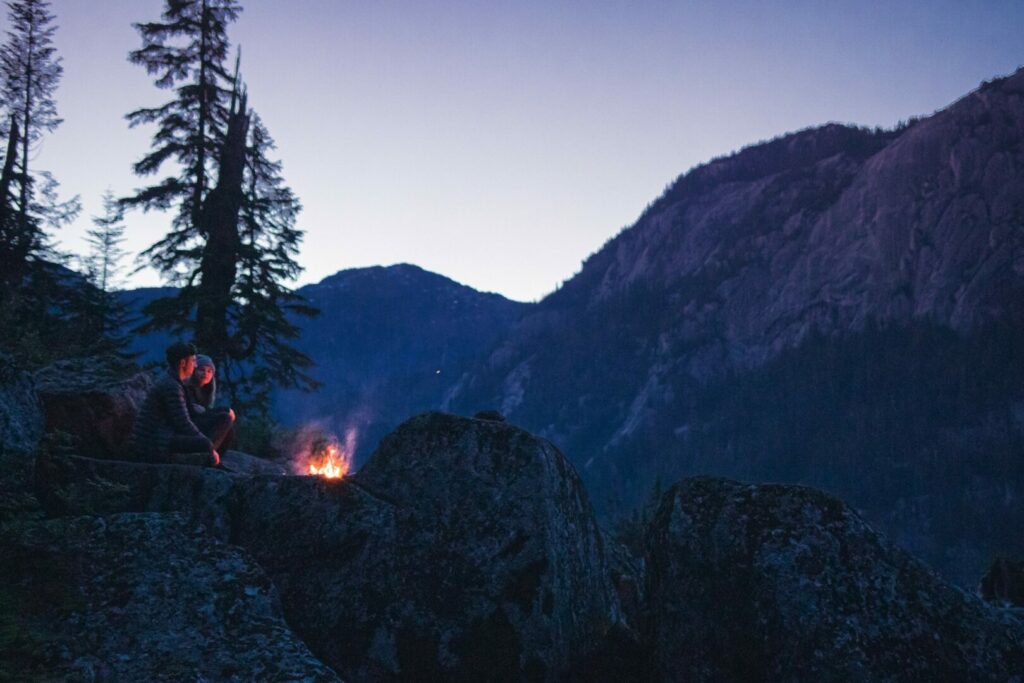 Couple sitting out in the mountains by their camping firewood