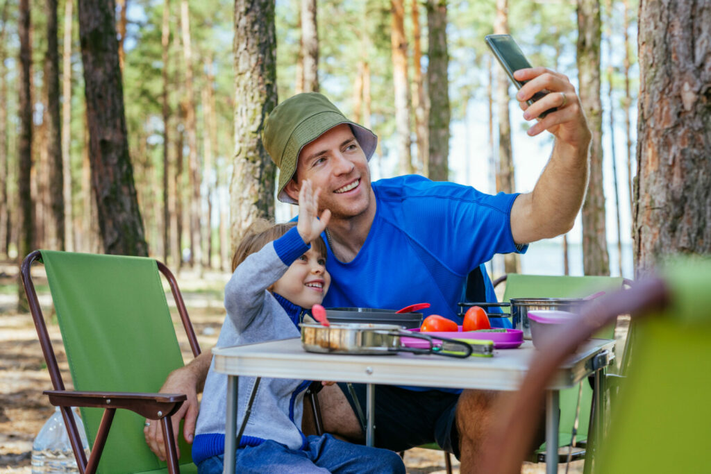 Father and a kid on the phone while sitting in their camping chairs