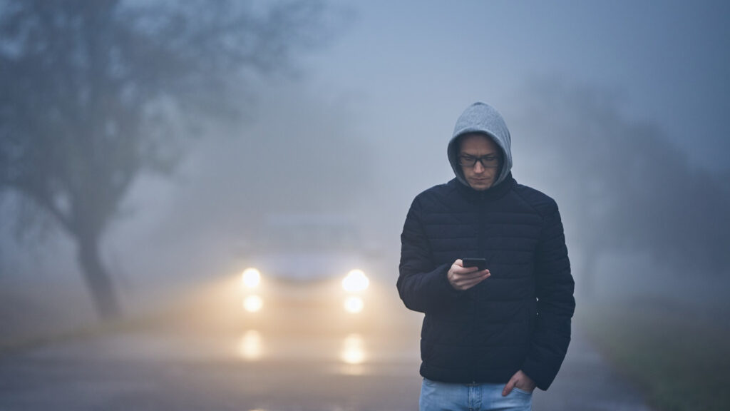 A man walking in the fog, where this driver should be slowing down when driving in fog to be safe.