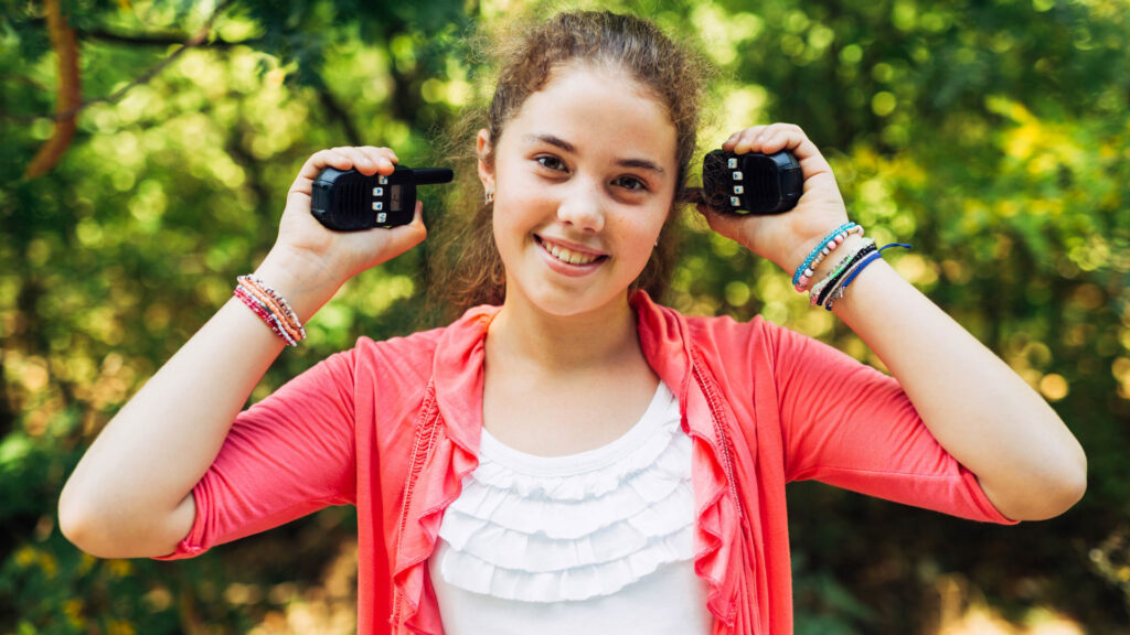 Girl holding two walkie talkies while playing in a camping scavenger hunt