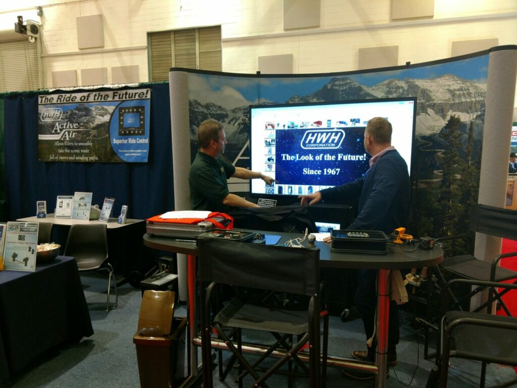 HWH Leveling employees setup in a booth at an RV show looking at the presentation on the screen behind them