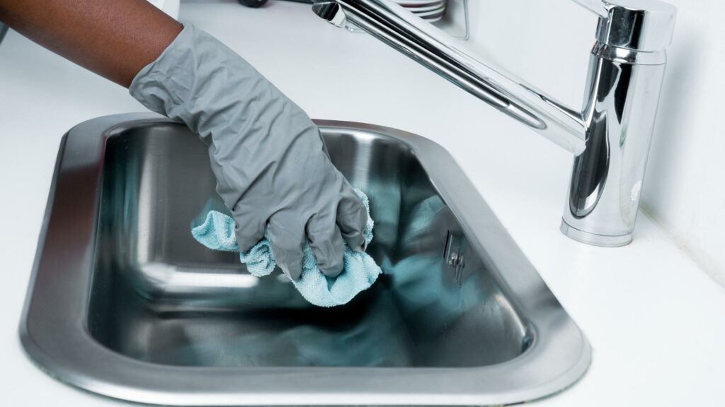 A woman using RV cleaning products to clean her stainless steel sink and faucet
